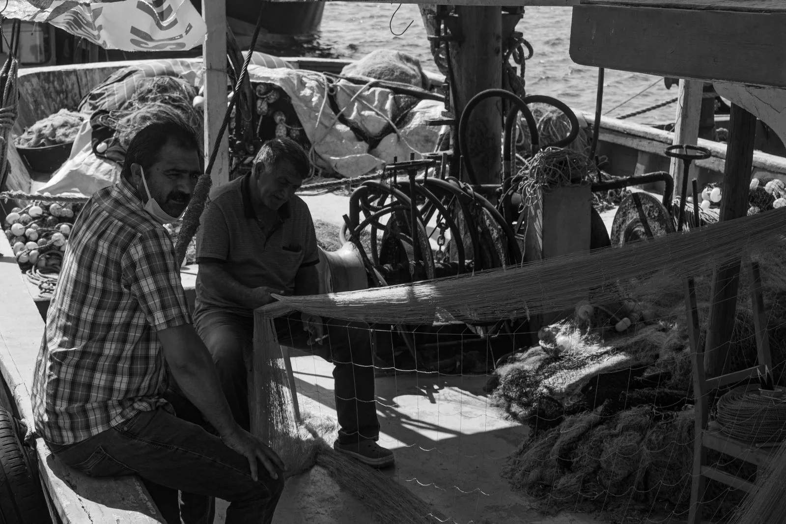 Two fishermen hauling nets on the deck of a trawler