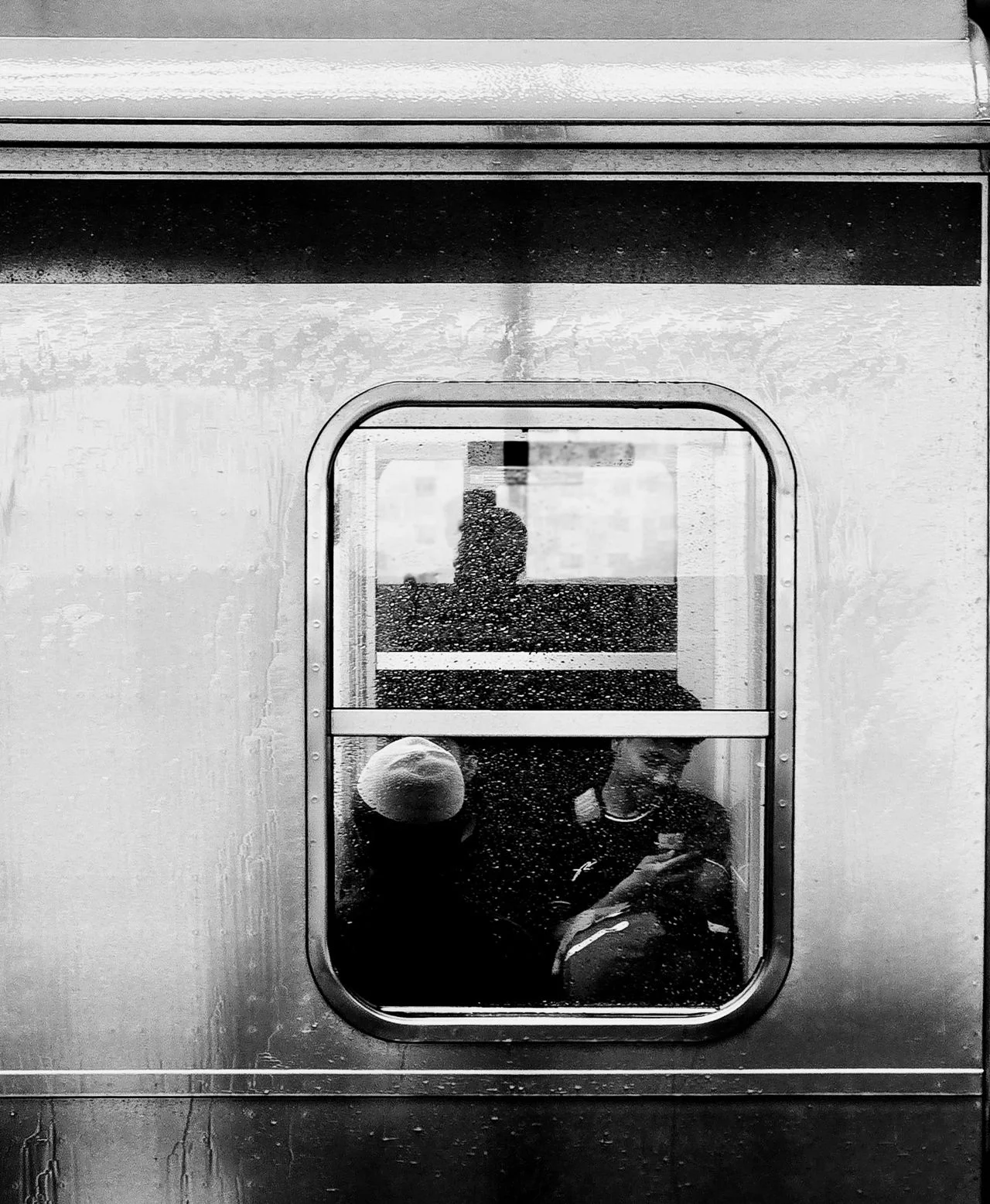 Passengers seen through a rain-streaked train window