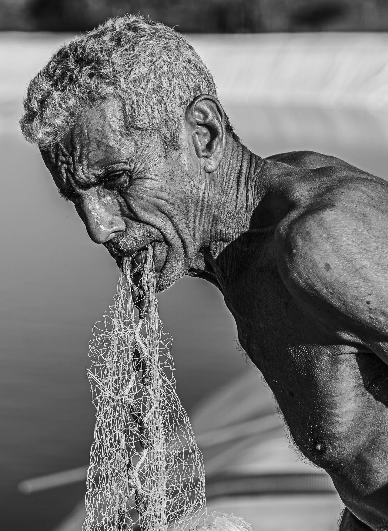 Senior fisherman mending a net, close-up portrait
