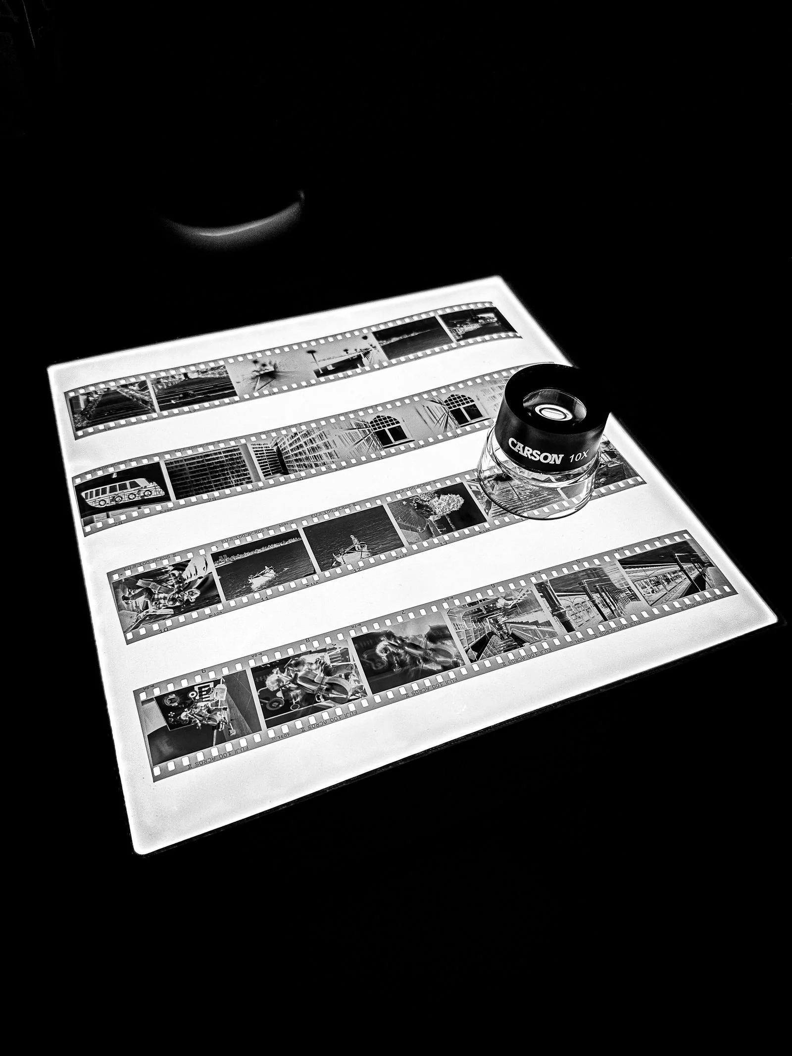 Strips of black-and-white 35 mm negatives on a lightbox, with a loupe