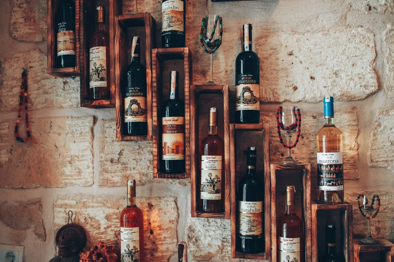 Bottles of natural wine on old wooden shelves against a stone wall